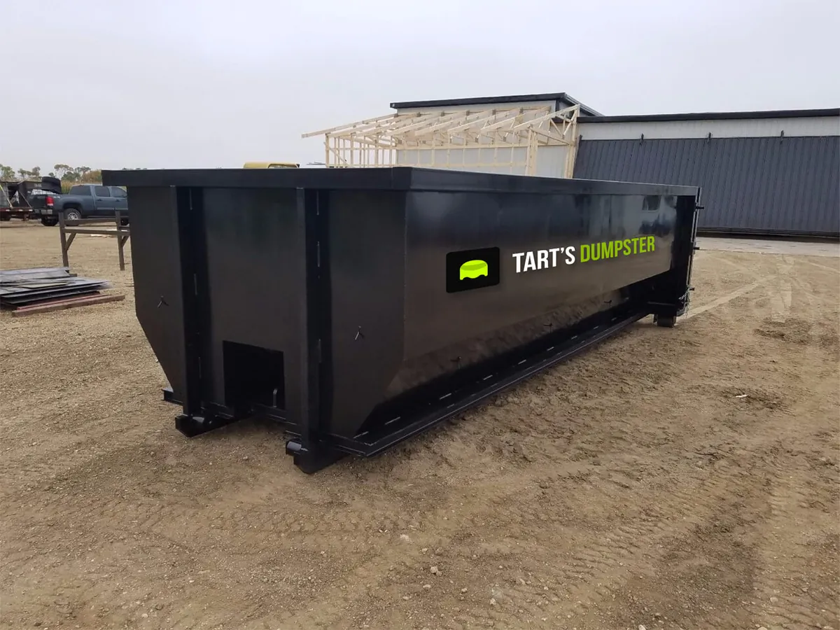 A black Tart’s Dumpster Service roll-off container on gravel